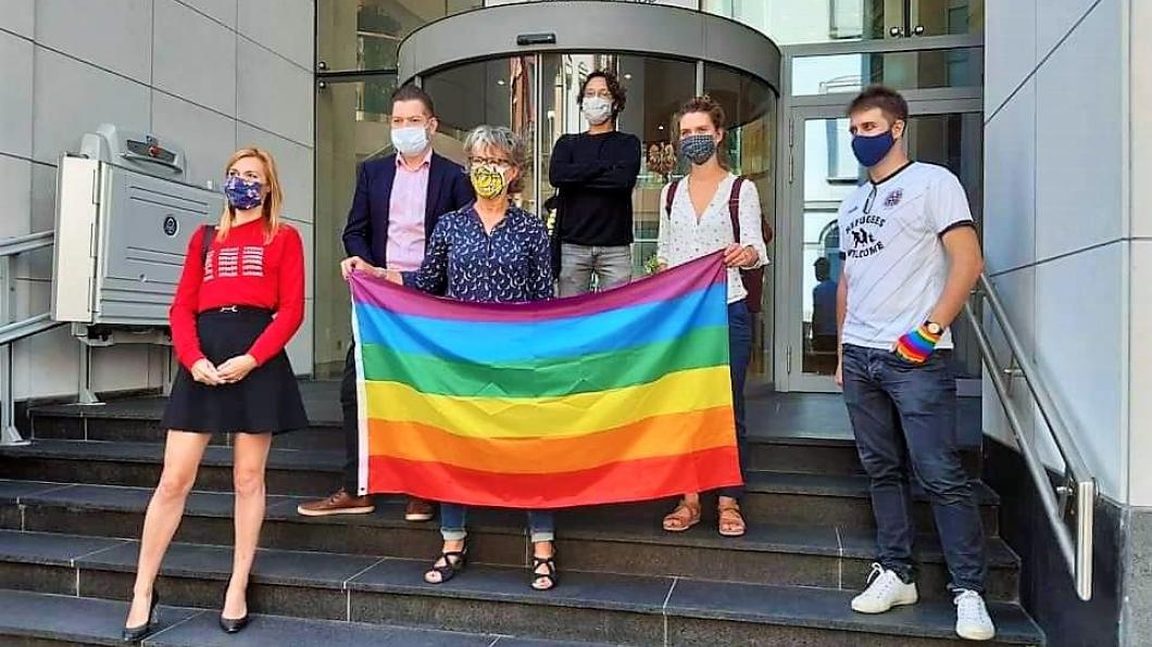 Kleine groep demonstranten met gezichtsmaskers op en regenboogvlag op de stoep van Poolse ambassade
