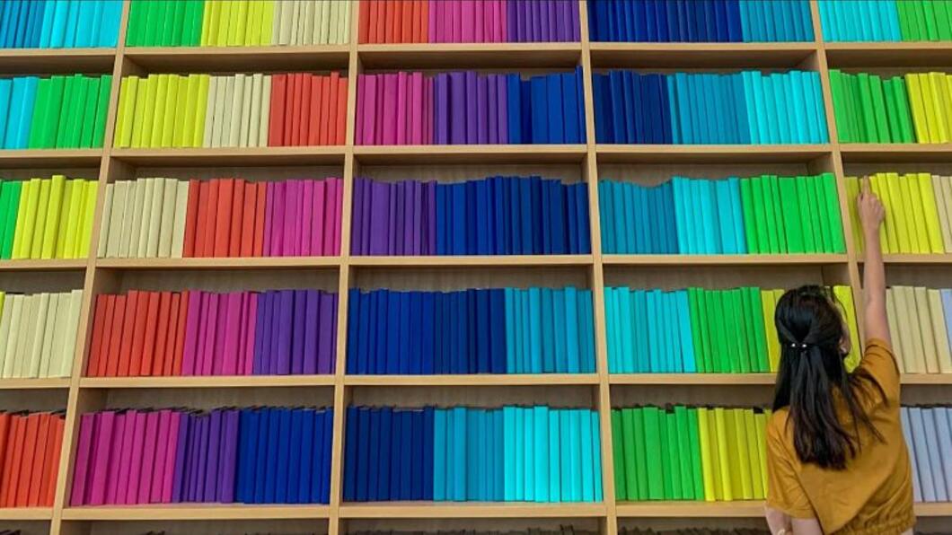 Boekenwand in regenboogkleuren met persoon die ieen boek wil pakken