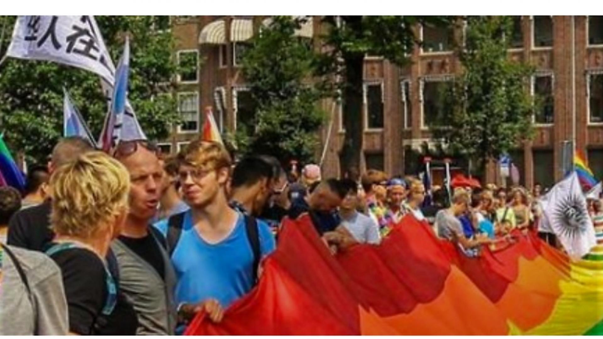 Beeld van mensen die met spandoeken en banners op de wal deelnemen aan Pride Amsterdam